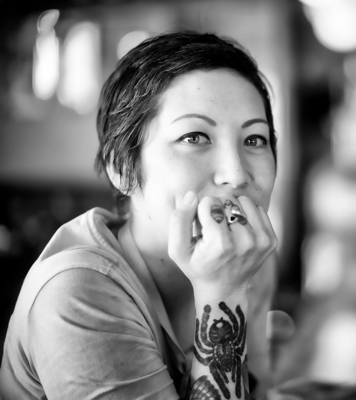 A woman with tattoos is sitting down and holding her hand to the mouth.